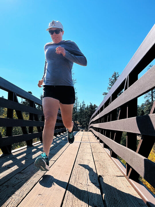 Woman running across a bridge in Evergreen Hilma Running shoes